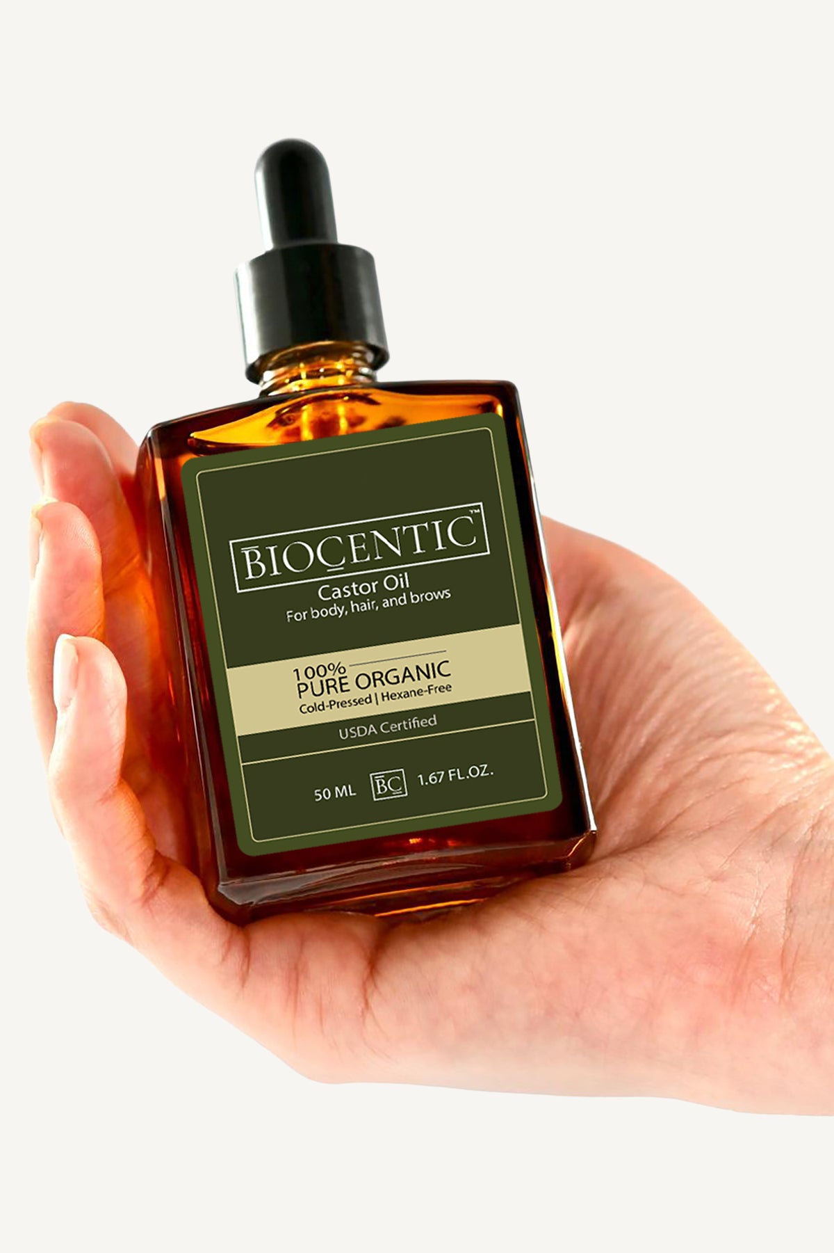 Hand holding a BIOCENTIC 50 mL amber glass castor oil bottle