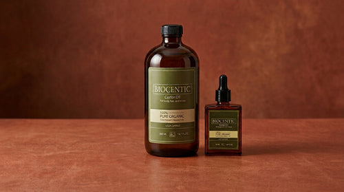 Amber glass bottles of BIOCENTIC castor oil on a warm reddish-brown ground.
